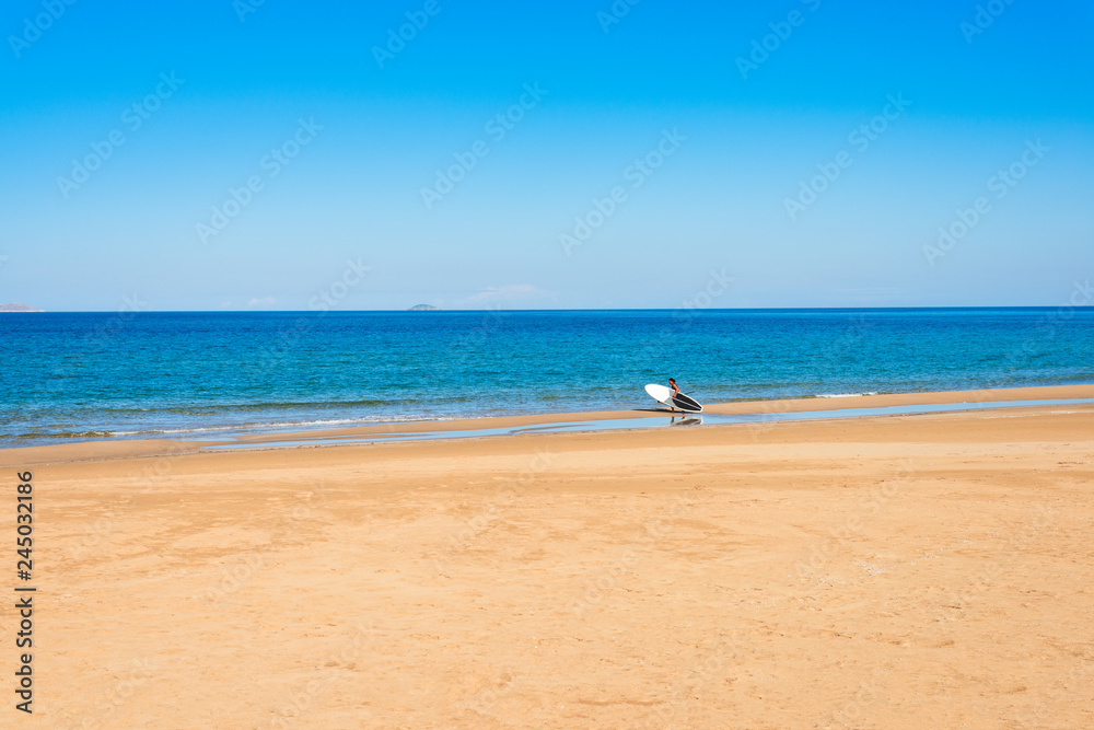 Paddleboard beach man holding paddle board walking on sand beach in summer morning. Mediterranean sea Arina sand beach water sports paradise.  Summer holidays vacation travel, Heraklion Crete Greece