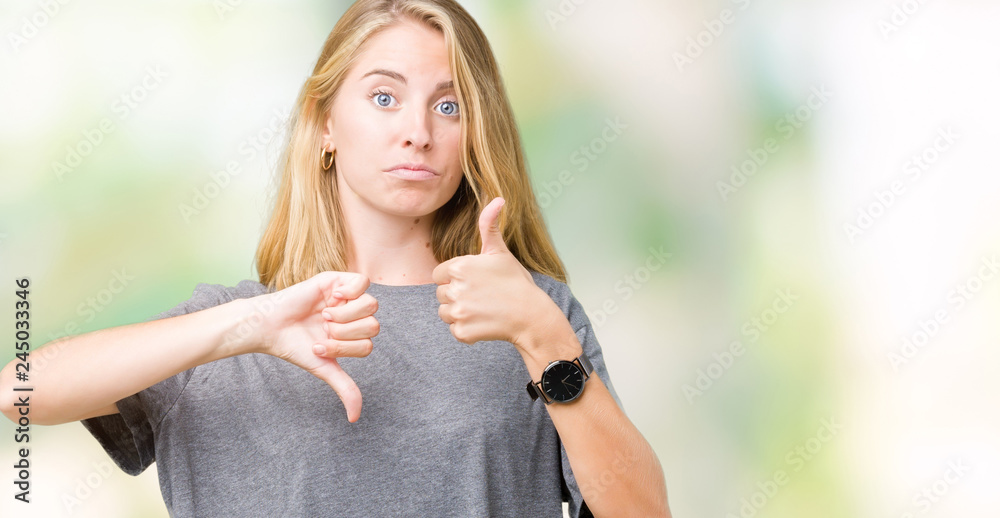 Obraz premium Beautiful young woman wearing oversize casual t-shirt over isolated background Doing thumbs up and down, disagreement and agreement expression. Crazy conflict