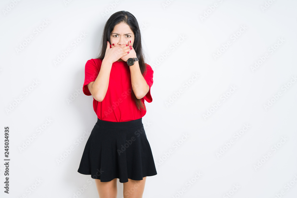 Beautiful brunette woman wearing red t-shirt and skirt over isolated background shocked covering mouth with hands for mistake. Secret concept. Beautiful brunette woman wearing red t-shirt and skirt over isolated background shocked covering mouth with hands for mistake. Secret concept.