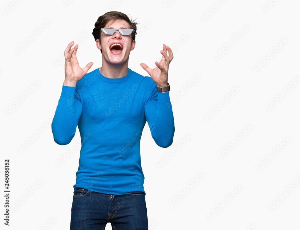 Young man wearing funny thug life glasses over isolated background celebrating mad and crazy for success with arms raised and closed eyes screaming excited. Winner concept Young man wearing funny thug life glasses over isolated background celebrating mad and crazy for success with arms raised and closed eyes screaming excited. Winner concept