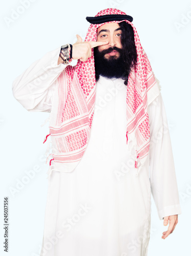 Arabian business man with long hair wearing traditional keffiyeh scarf Pointing with hand finger to face and nose, smiling cheerful