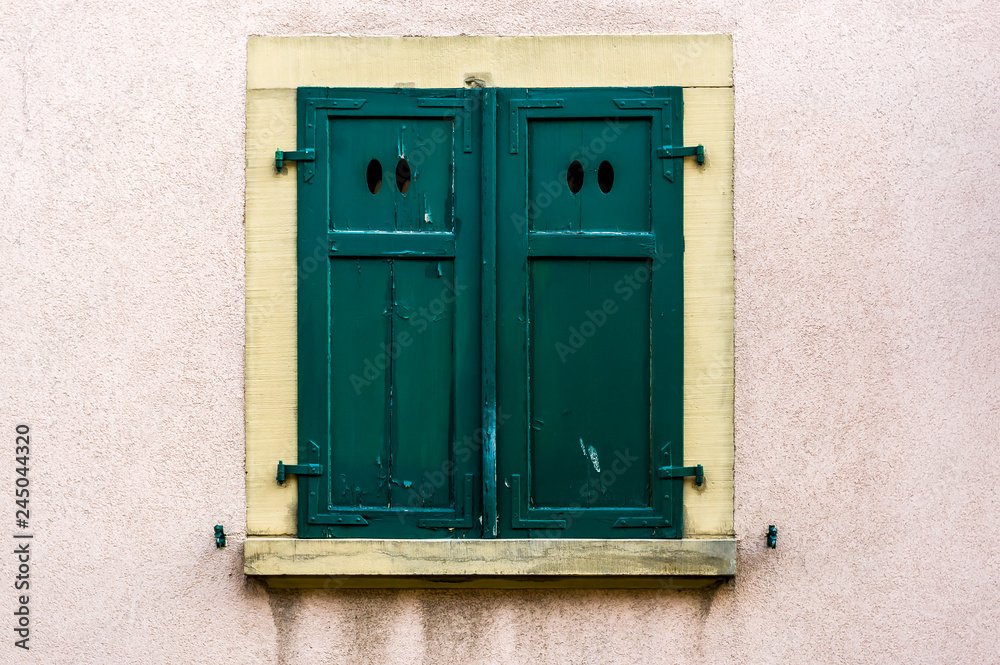 Hausfassade mit grünem geschlossenem Fensterladen aus Holz mit 4 ovalen Lichtöffnungen