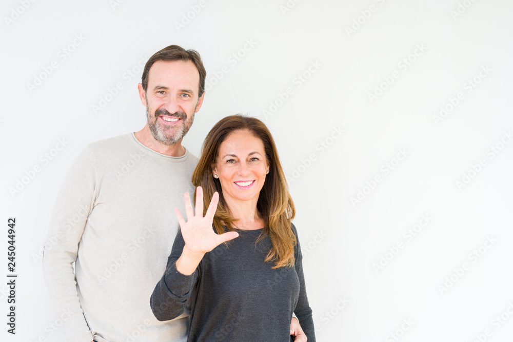 Beautiful middle age couple in love over isolated background showing and pointing up with fingers number five while smiling confident and happy.