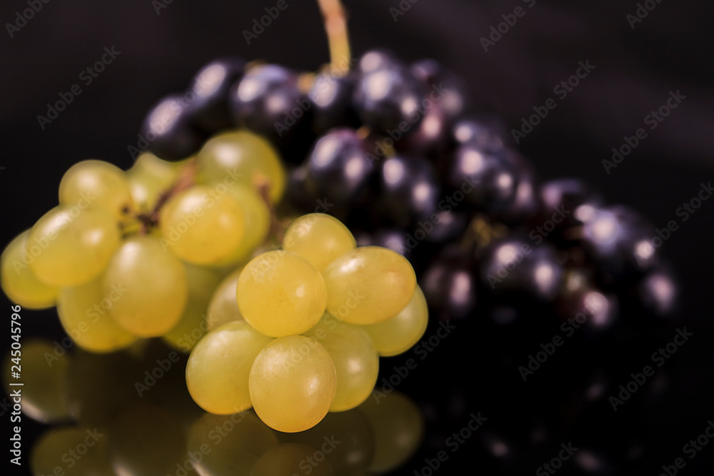 Close-up, berries of dark and yellow bunch of grape in low light mirror black background Close-up, berries of dark and yellow bunch of grape in low light mirror black background