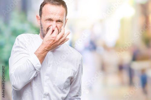 Middle age hoary senior man over isolated background smelling something stinky and disgusting, intolerable smell, holding breath with fingers on nose. Bad smells concept.