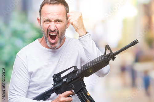 Middle age senior hoary criminal man holding gun weapon over isolated background annoyed and frustrated shouting with anger  crazy and yelling with raised hand  anger concept