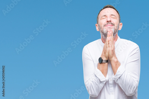 Middle age hoary senior man over isolated background praying with hands together asking for forgiveness smiling confident.