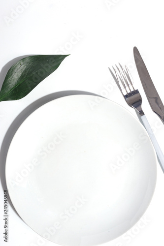 White plate and cutlery on a light table. Cretive minimalistic concept.