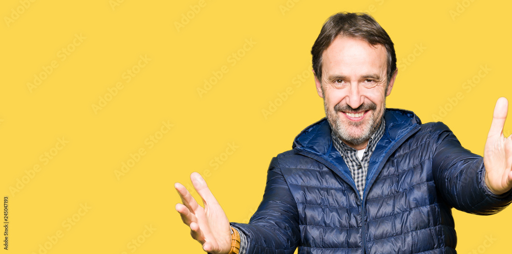 Middle age handsome man wearing winter coat looking at the camera smiling with open arms for hug. Cheerful expression embracing happiness. Middle age handsome man wearing winter coat looking at the camera smiling with open arms for hug. Cheerful expression embracing happiness.