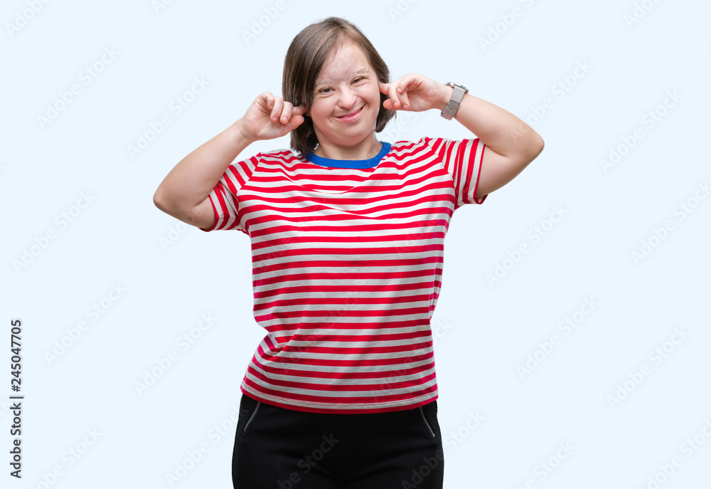 Young adult woman with down syndrome over isolated background covering ears with fingers with annoyed expression for the noise of loud music. Deaf concept.