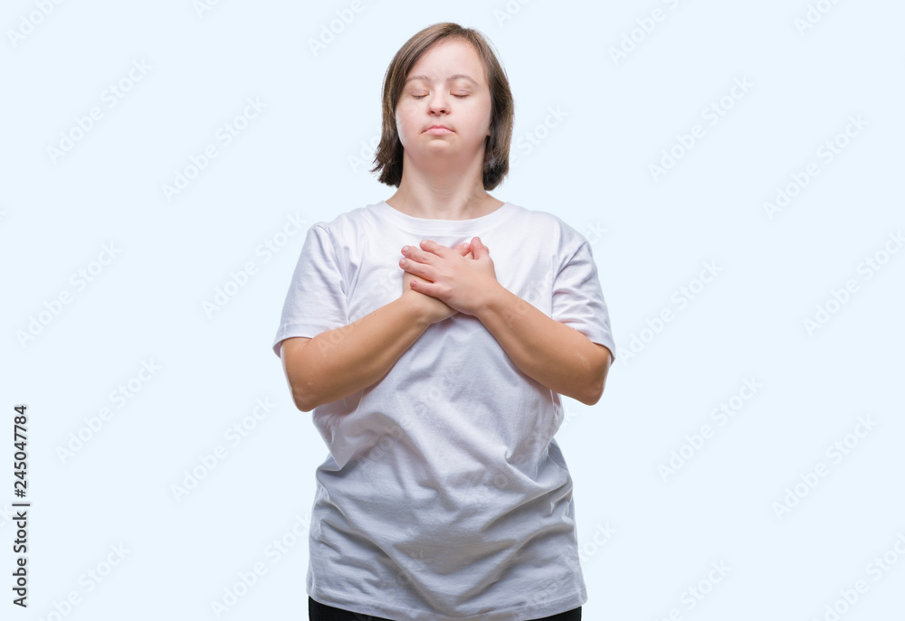 Young adult woman with down syndrome over isolated background smiling with hands on chest with closed eyes and grateful gesture on face. Health concept. Young adult woman with down syndrome over isolated background smiling with hands on chest with closed eyes and grateful gesture on face. Health concept.