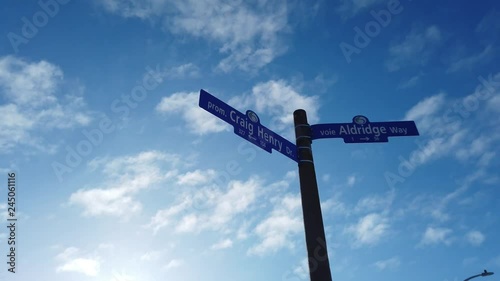 Looking up at a blue street sign that says Craig Henry and Aldridge before a blue sky in slow motion photo