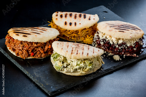 Venezuelan Latin American food, 4 arepas of different stuffing on a black table. Arepa with mechada meat, queen pepeada, black beans with white cheese and chicken