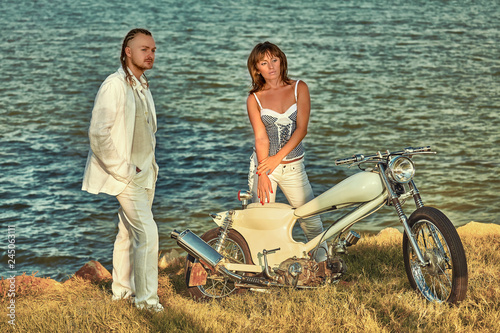 Young romantic couple with vintage custom motorbike on the tropical coast background.
