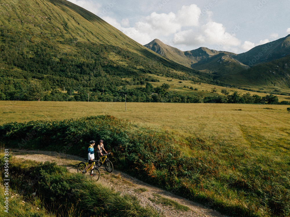 Fototapeta premium Couple cycling down a road in the Scottish Highlands