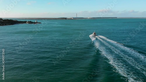 Following commercial boat on blue ocean beautiful sunny day with lighthouse and coast in the background - Bluff, New Zealand - Aerial Drone photo