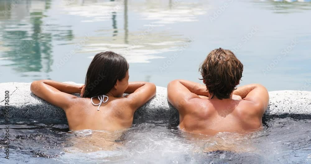 Spa couple happy in wellness hot tub jacuzzi laughing having fun being in love. Happy young lovers on honeymoon vacation travel to luxury resort spa retreat. Handsome man and beautiful asian woman.