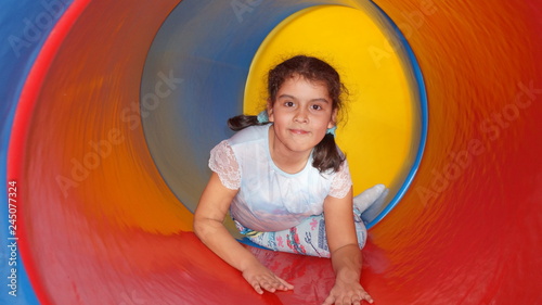 Little girl in a colored spiral tube on a playground for children, photo of a plastic pipe with curves, view from the inside