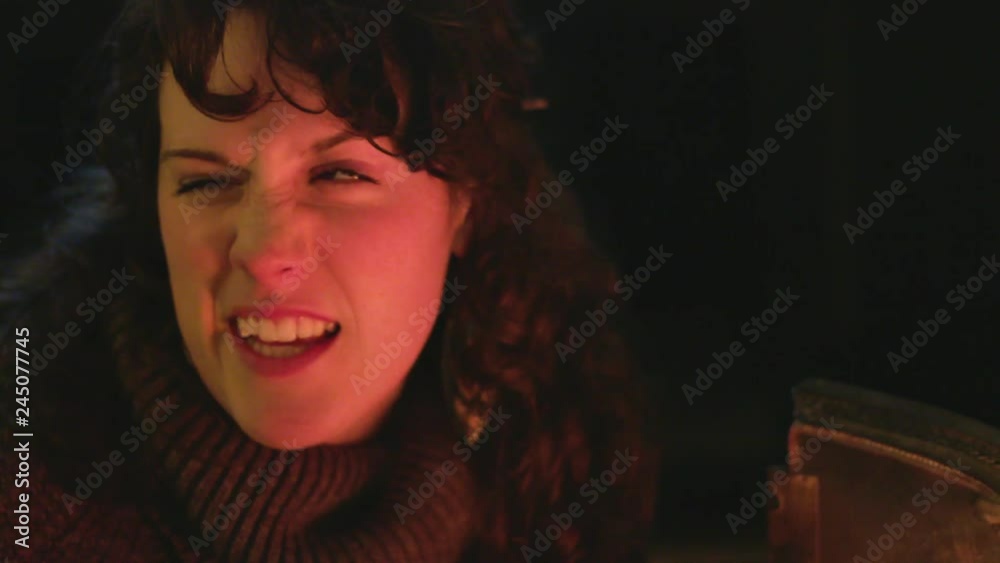 Happy young woman talks to friend as fire from fireplace flickers on her face. Happy young woman talks to friend as fire from fireplace flickers on her face.