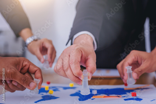 Hand of businesspeople playing chess with world map as a board. Business strategy concept.