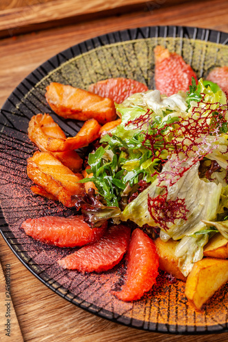 Modern Arabic cuisine in 2019. Asian salad of fried salmon, avacado, grapefruit and salad mix, with honey sauce. Serving dishes in a restaurant in a black plate with oriental spices.
