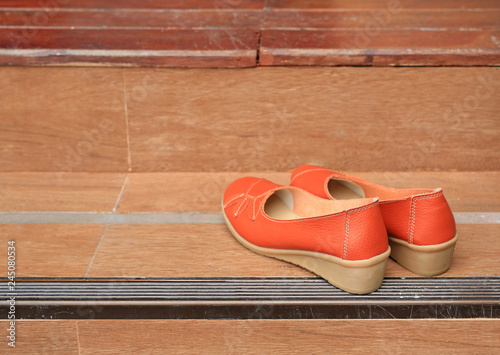 Orange leather female shoes place on wood stair.