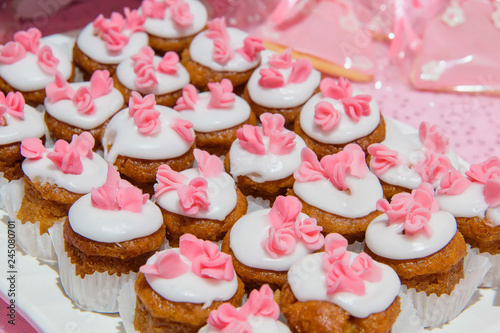 Brown cupcakes with white cream and pink flowers. Round little cookies on a plate. Cupcakes in white paper form. Pastry for tea. Sponge cakes. photo