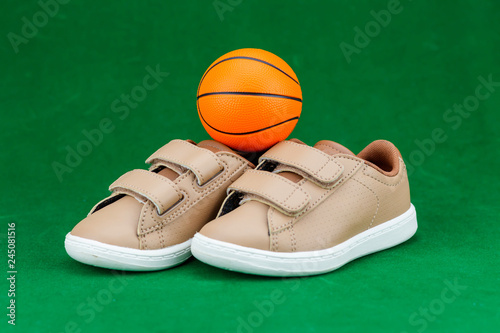 Concept encourage children to play sport  exercise for a healthy body  shoes of small baby shoes next to ball isolated on green background.