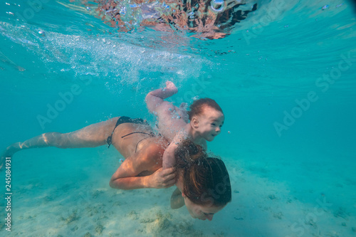 Happy mother playing with infant boy in beautiful tropical sea water with white sand, activity in vacation, underwater shot at Maldives, baby diving underwater
