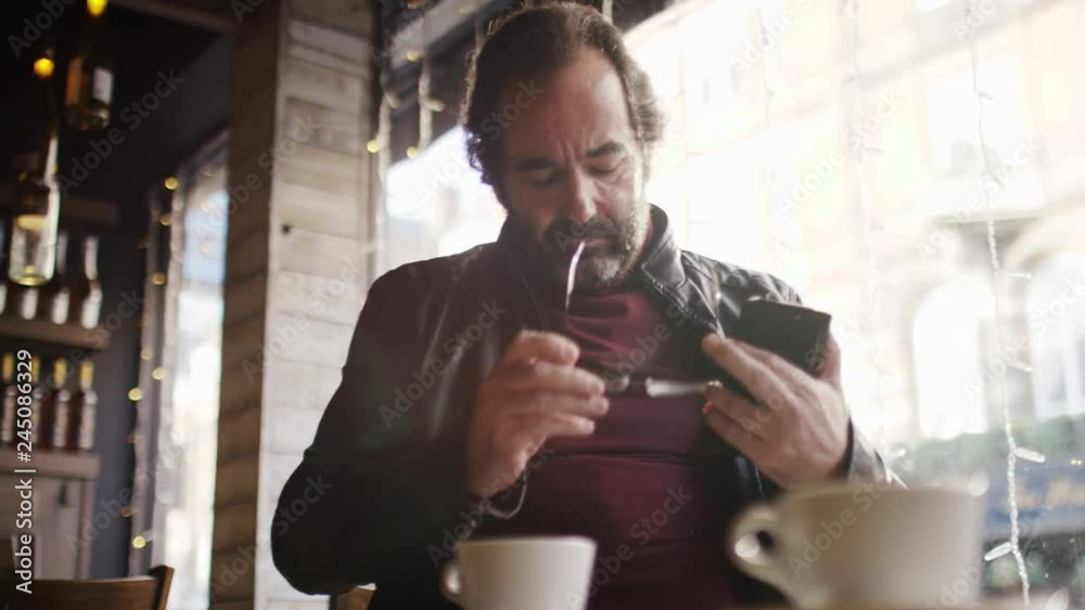 Affluent confident man checking his phone as he enjoys a morning coffee, in slow motion