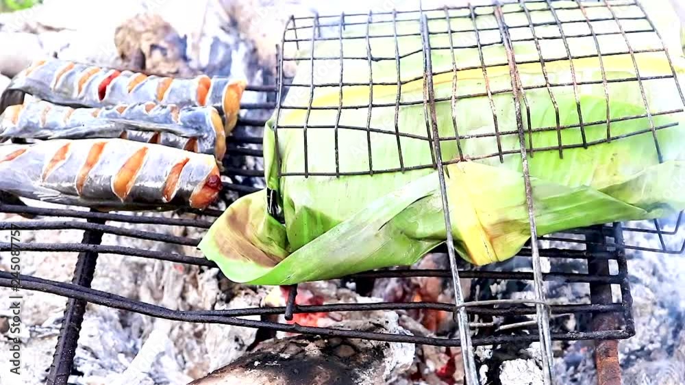 Cooking catfish fish wrapped in banana leaves on an open hot fire in