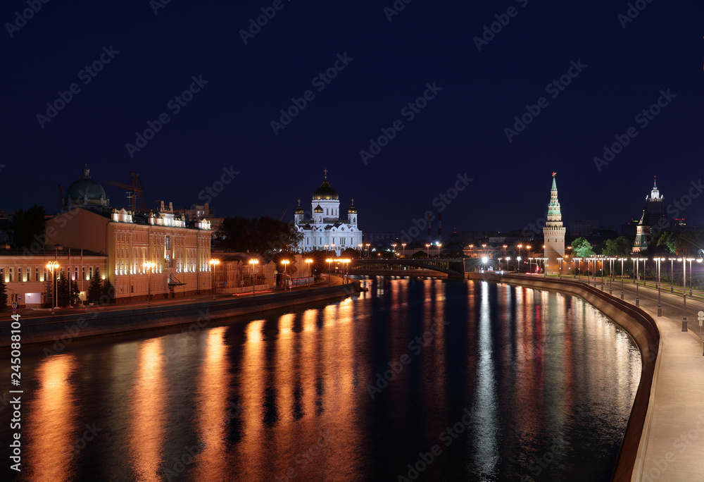 View of a Moscow at night from Bolshoy Moskvoretskiy bridge. View at  Kremlevskaya and Sofiyskaya embankments. Vodovzvodnaya tower, Cathedral of Christ the Saviour, reflections on Moskva river.