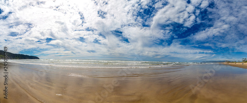 Wide angle panorama of a Cape Meares beach. Clouds in dramatic sky reflects on a wet surface of a beach at a low tide