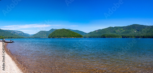 Scenic panorama of Detroit Lake, Oregon. Blue crystal clear water, sky with clouds small island in the middle and a fishing boat on a lake beach