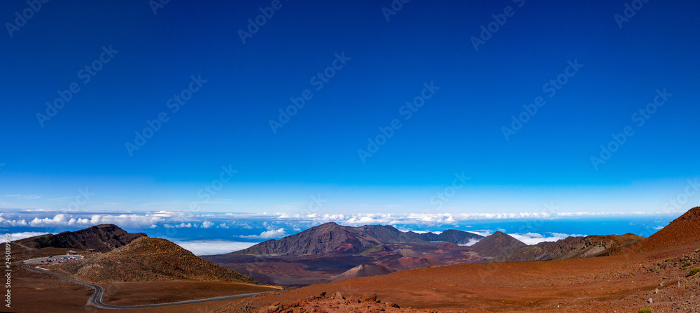 Scenic panorama of a Haleakala volcano. Clear blue sky white puffy clouds below the horizon and rich red-brown colors of a mountain 