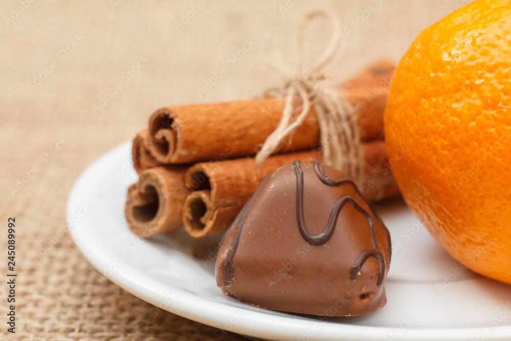 Chocolate candy on white plate with cinnamon and orange. Chocolate candy on white plate with cinnamon and orange.