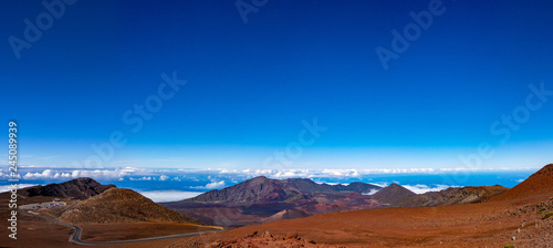 Scenic panorama of a Haleakala volcano. Clear blue sky white puffy clouds below the horizon and rich red-brown colors of a mountain 