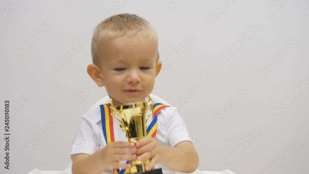Proud baby child looking to champion cup, smiling blue eyes, blond hair kid Proud baby child looking to champion cup, smiling blue eyes, blond hair kid