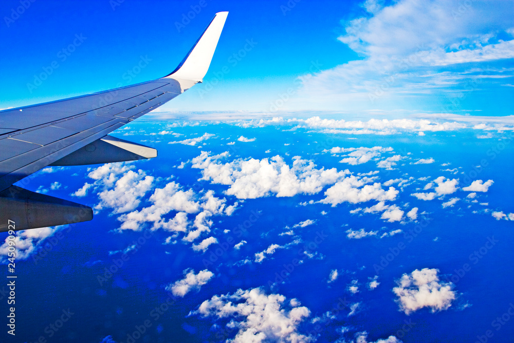 wing of an airplane on a blue sky with cumulus clouds from an airplane window wing of an airplane on a blue sky with cumulus clouds from an airplane window
