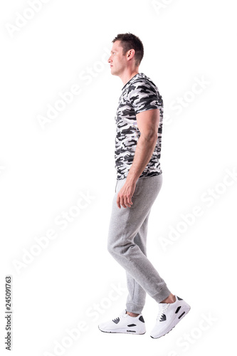 Profile view of young fit man in sport clothes walking confident and looking ahead. Full body isolated on white background.
