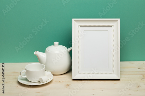 white frame with cup and teapot on white desk near green wall
