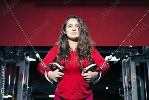 Young beautiful athletic girl trains on the simulator in the gym. sporty woman in red leggings doing exercise
