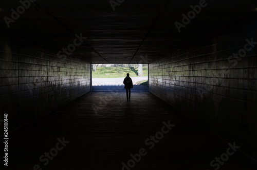 silhouette of a person walking through a dark underpass symbolizing light at the end of the tunnel