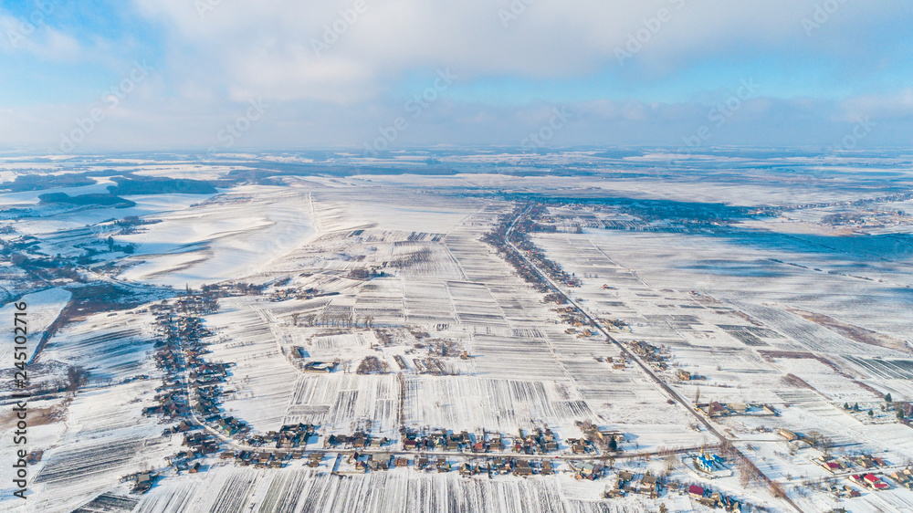 Aerial view of winter land with forests, white fields, in winter on an overcast day.