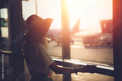 Young woman tourist in straw hat writes messages via smartphone at airport near terminal. Travel concept photo