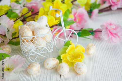 Multicolored easter eggs and flowers on white wooden background