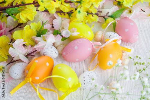 Multicolored easter eggs and flowers on white wooden background