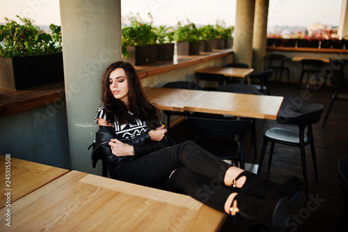Young curly woman in leather jacket in a bar put her legs on table. © AS Photo Family