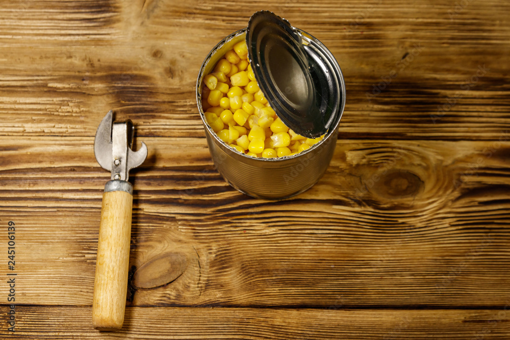 Open tin can of corn and can opener on wooden table Open tin can of corn and can opener on wooden table