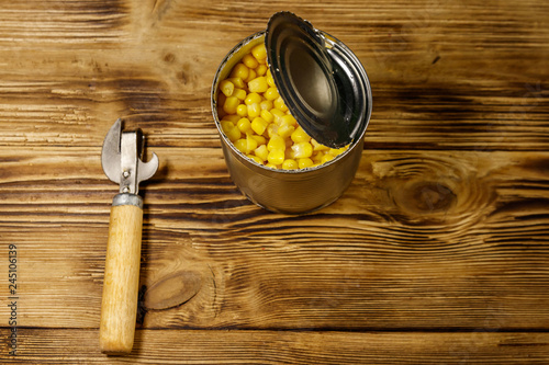 Open tin can of corn and can opener on wooden table